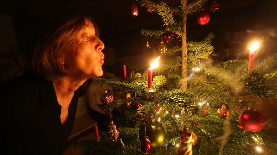 Eine Frau bläst an einem Weihnachtsbaum eine Kerze aus