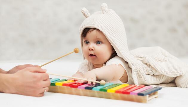 Baby, das am Glockenspiel sitzt und Mutter zusieht. 