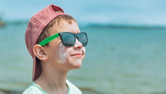 Junge am Strad mit Sonnencreme im Gesicht