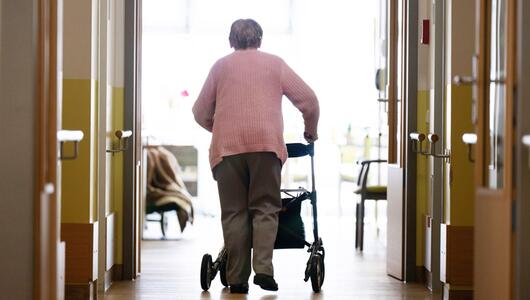 Eine Frau geht mit einem Rollator in einem Altenheim