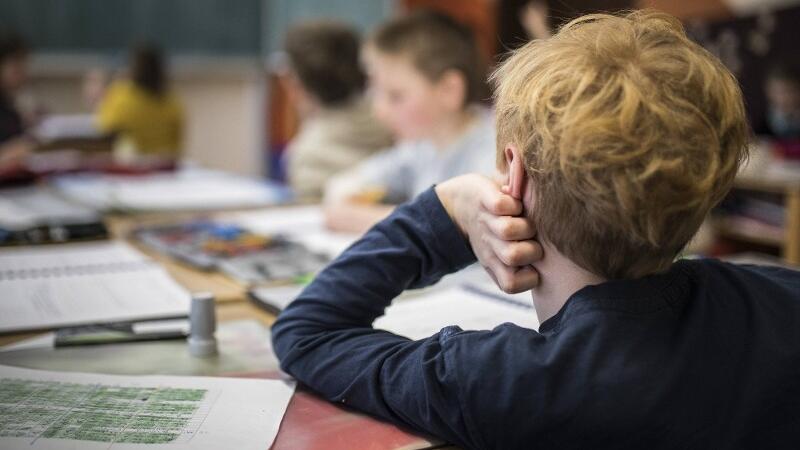 Ein junger Schüler sitzt gelangweilt an seinem Tisch.