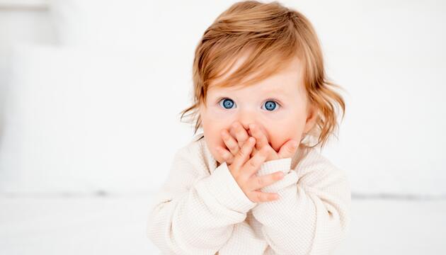 Rothaariges Kleinkind, das sich die Hände vor den Mund hält