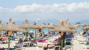 Urlauber liegen auf Strandliegen unter Sonnenschirmen. Im Hintergrund ist Meer zu sehen.