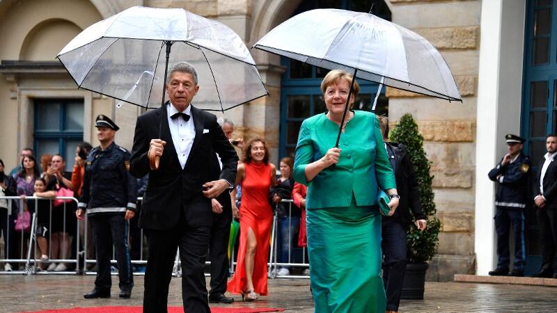 Angela Merkel hat ein grünes Kleid an und einen Regenschirm in der Hand.