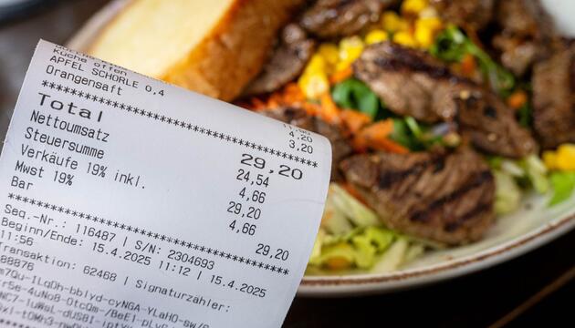 Eine Rechnung mit Mehrwertsteuer neben einem vollen Teller in einem Restaurant. 