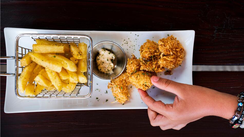 Hand greift ein Stück frittiertes Hühnchen.