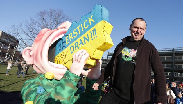 Jacques Tilly steht neben seiner Figur, die Putin zeigt, wie er an der Ukraine erstickt.