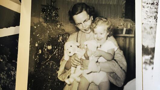 Altes Polaroid einer Mutter, die ein Kind auf dem Arm hält, dahinter ein Weihnachtsbaum. 