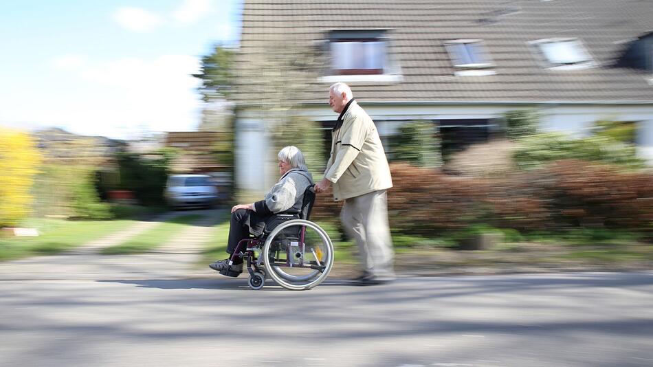 Mann schiebt seine Frau im Rollstuhl durch ein Wohngebiet