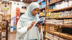 Muslimische Frau in einem Supermarktgang prüft via App, ob die Lebensmittel halal sind.