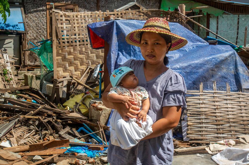 Eine Mutter mit ihrem Baby vor einem zerstörten Haus