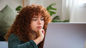 Junge Frau mit roten Locken, die vor Laptop sitzt. 