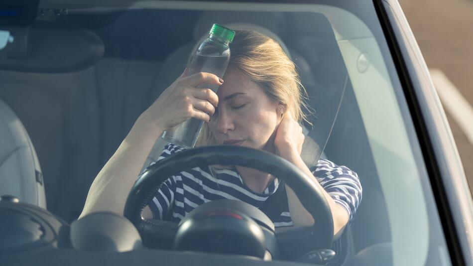 Frau sitzt im Auto und kühlt ihren Kopf mit einer Wasserflasche