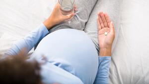 Schwangere Frau, die eine Tablette in der einen und ein Wasserglas in der anderen Hand hält