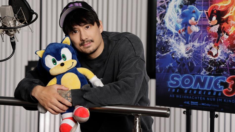 Julien Bam hält den blauen Igel Sonic im Arm, dem er seine prominente Stimme leiht.