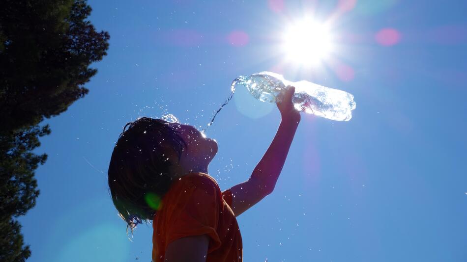 Kind kippt sich Wasser über den Kopf, die Sonne steht hoch am Himmel