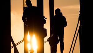 Zwei Männer gehen mit Aktentasche bei Sonnenaufgang über Brücke