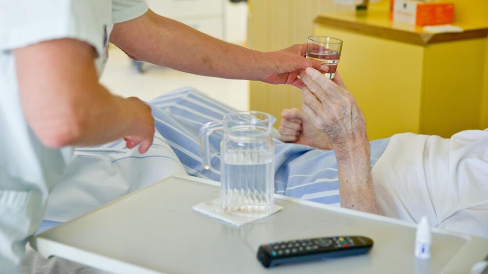 Eine Krankenpflegerin reicht einem Patienten ein Glas Wasser.