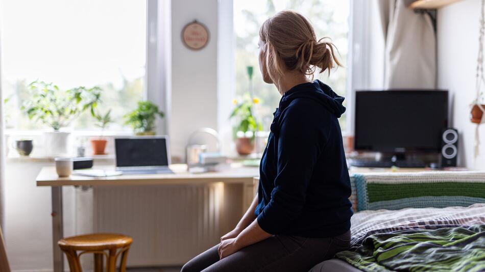 Eine Studentin sitzt auf dem Bett in ihrem WG-Zimmer