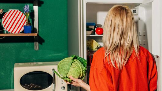 Eine Frau hält einen Kohl vor einem offenen Kühlschrank
