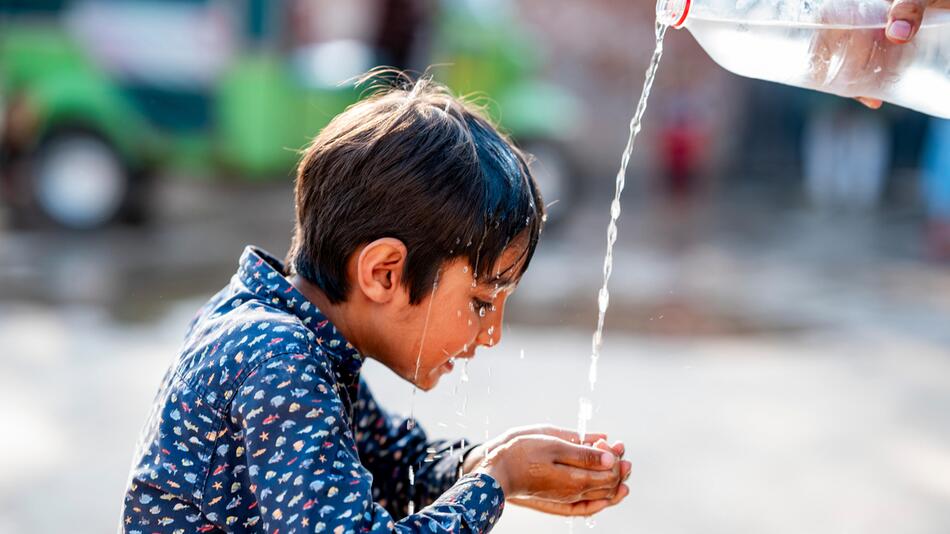 Einem kleinen Jungen wird Wasser aus einer Flasche in die Hände geschüttet