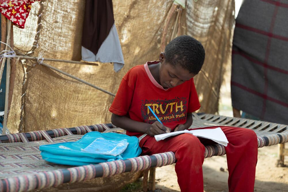 Ein Junge mit Schulsachen auf einer Pritsche