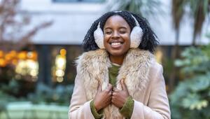Eine Frau in Pullover, Jacke mit Fellkragen und Ohrenwärmern lächelt.