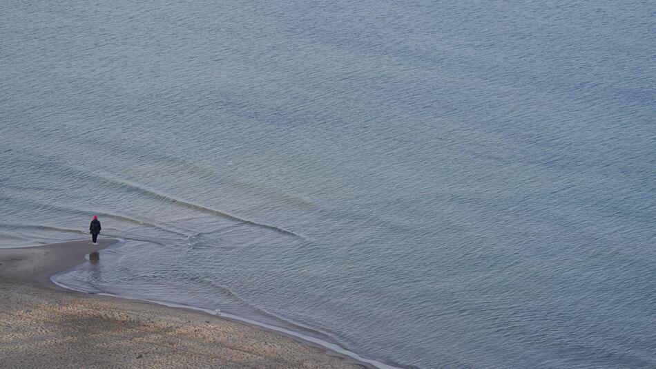 Eine Frau steht allein am Strand der Ostsee