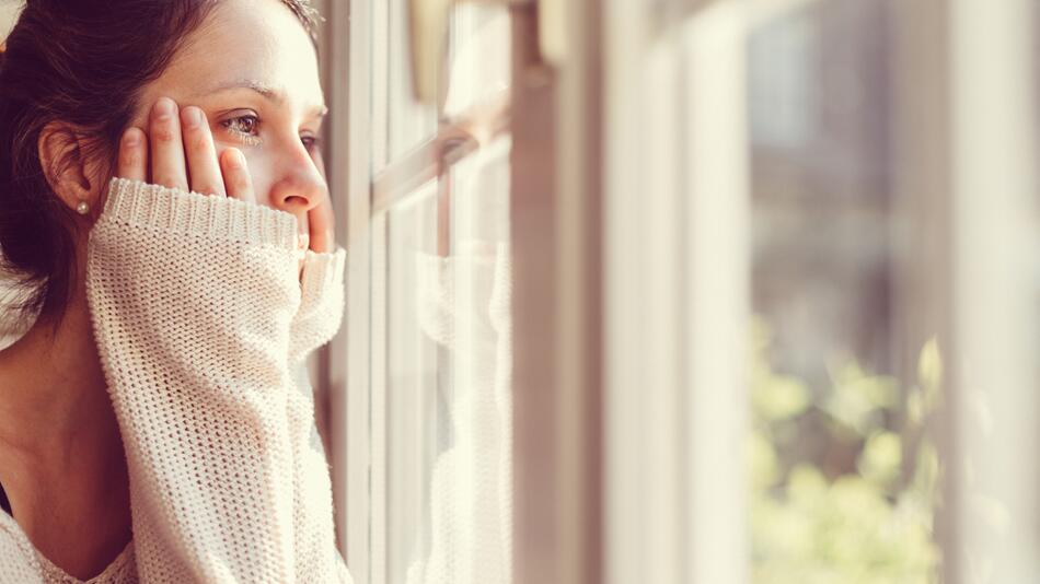 Frau blickt gedankenverloren aus dem Fenster